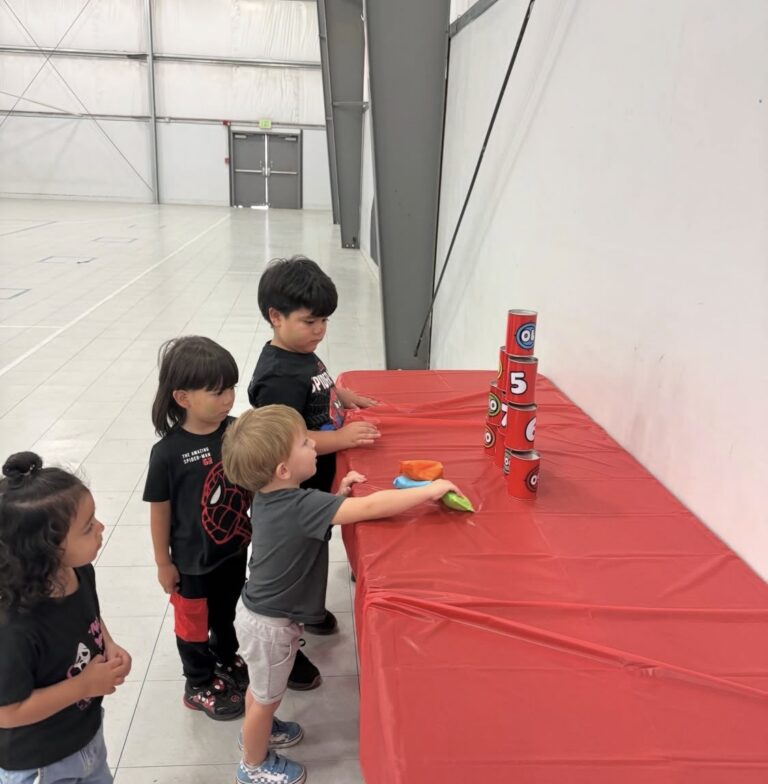 Children playing a beanbag game with stacked cans in the gym