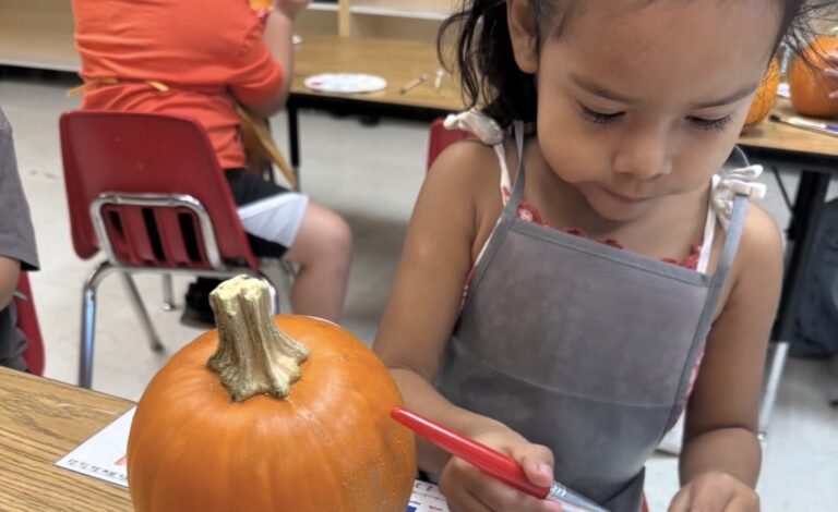A child painting a pumpkin with a red paintbrush