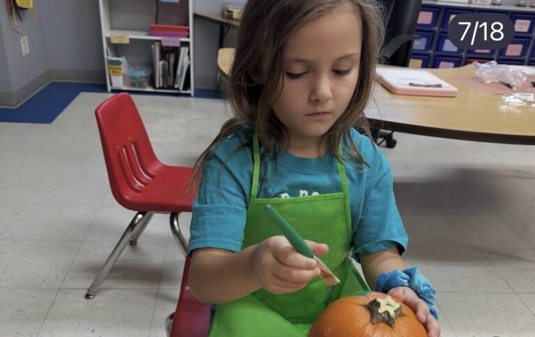 A child painting a pumpkin while wearing a green apron
