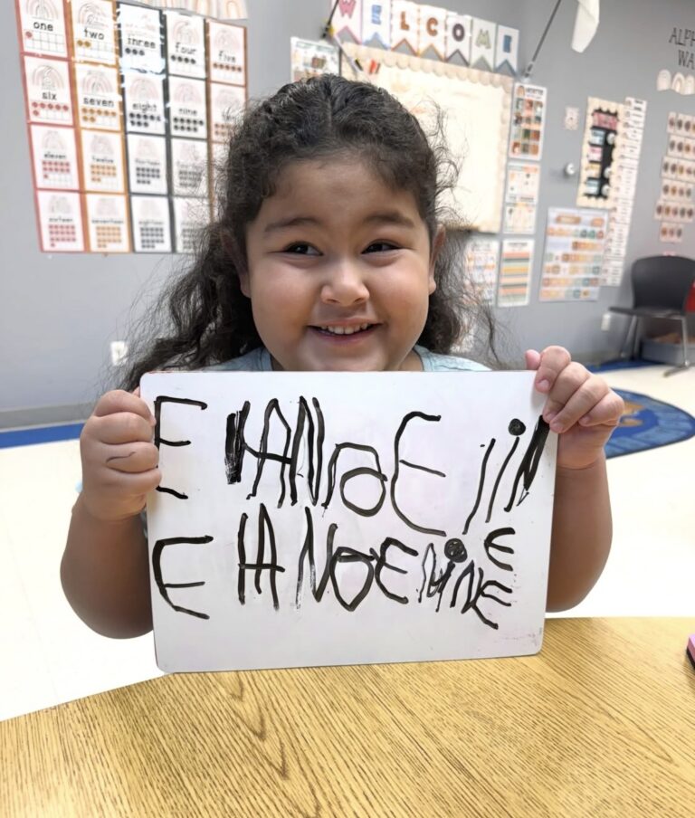 A child proudly holding a classroom writing board