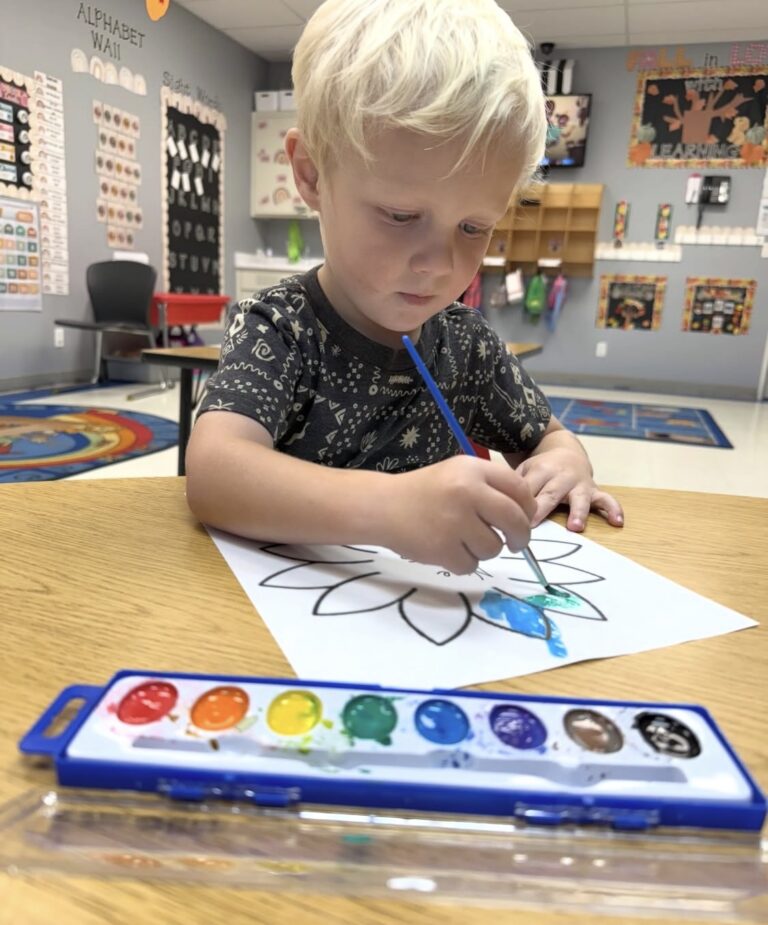 A child painting a flower with watercolors in the classroom
